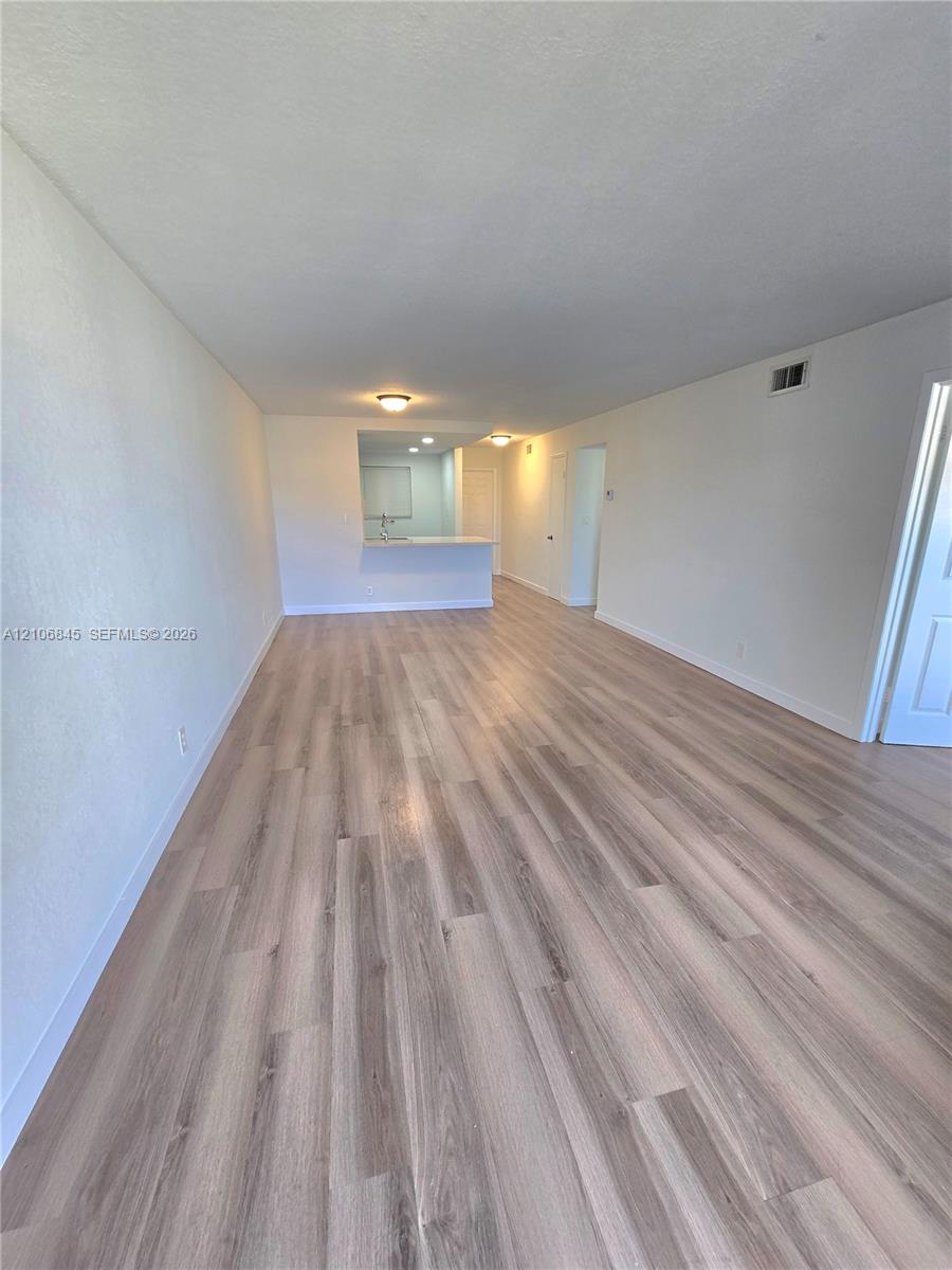 Open-concept interior featuring light-toned wood-finish flooring, neutral walls, flush-mount ceiling lighting, and a kitchen pass-through counter