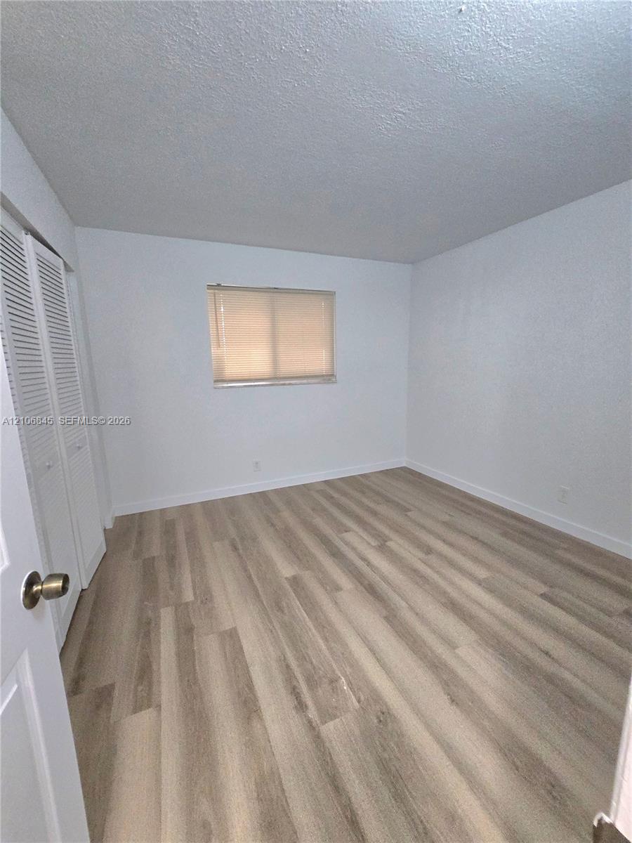 Neutral-toned wood-finish flooring, white walls, and a built-in closet with louvered doors