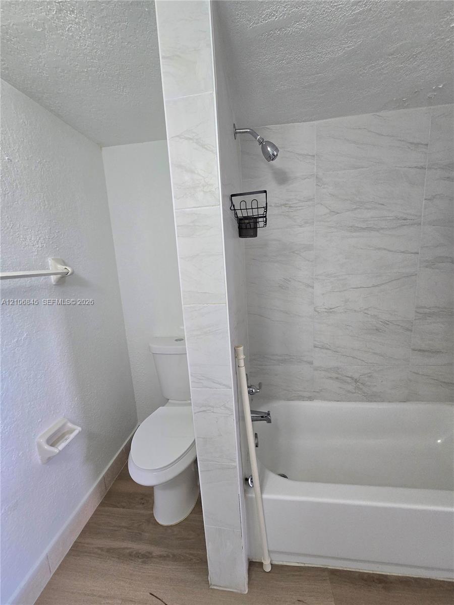 Bathroom featuring a porcelain-tiled shower surround, integrated bathtub, wall-mounted toilet, and wood-finish flooring