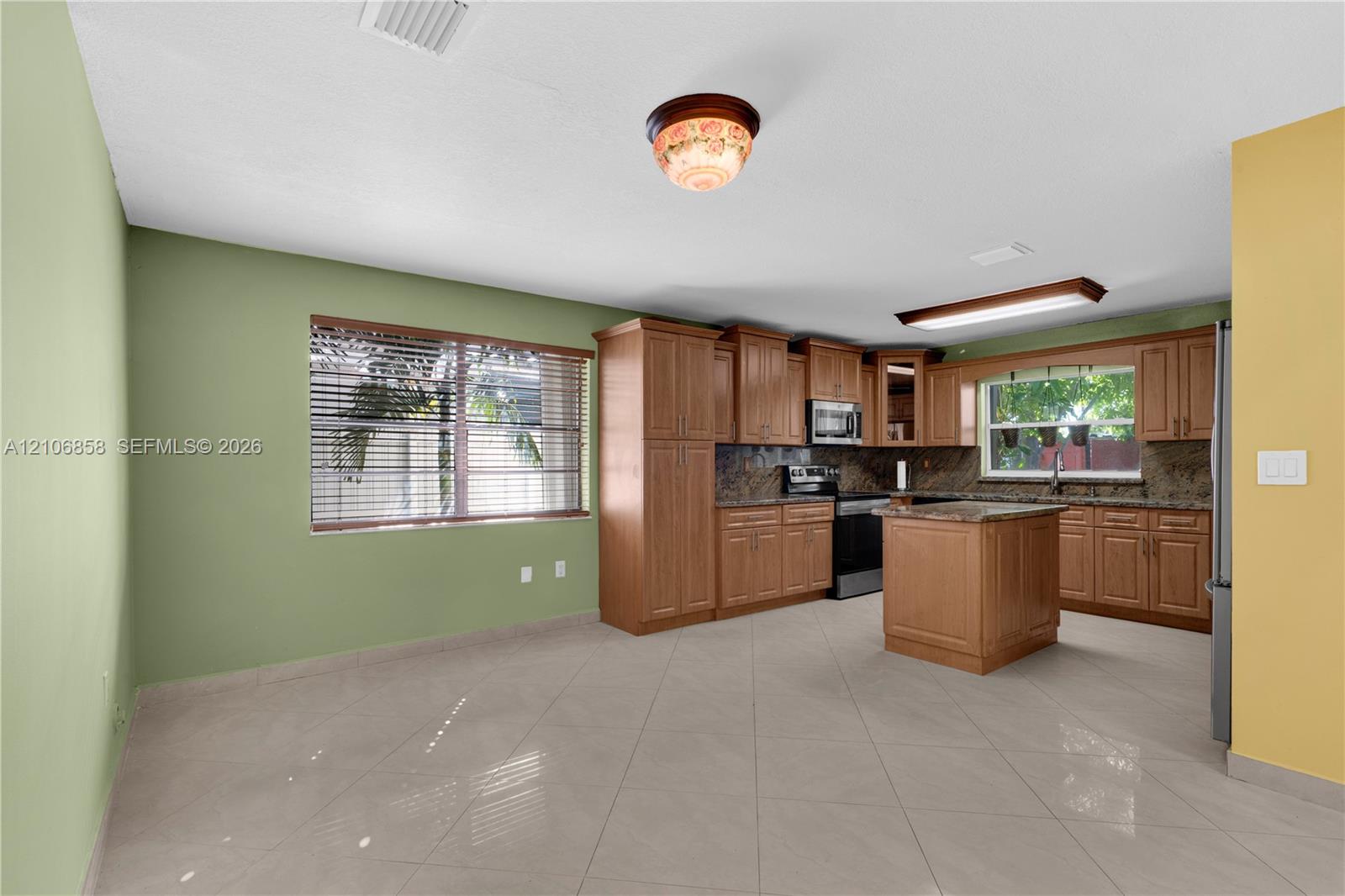 Kitchen featuring wood cabinetry, stone countertops, central island, tile flooring, and integrated stainless steel appliances Kitchen featuring wood cabinetry, stone countertops, central island, tile flooring, and integrated stainless steel appliances