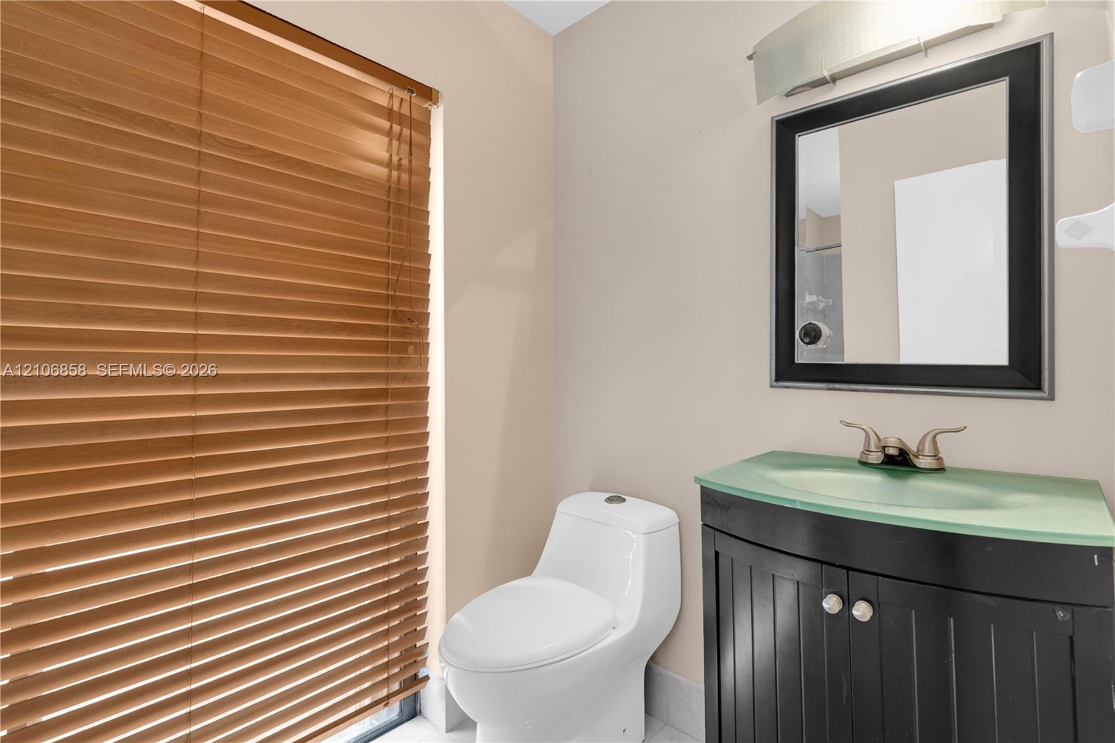 Vanity cabinet with a molded integrated sink and countertop, framed wall mirror, polished metallic fixtures, and wood-finish window blinds