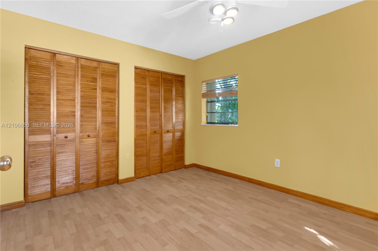 Wood-finish flooring, two sets of bifold wooden closet doors, and a ceiling-mounted light fixture