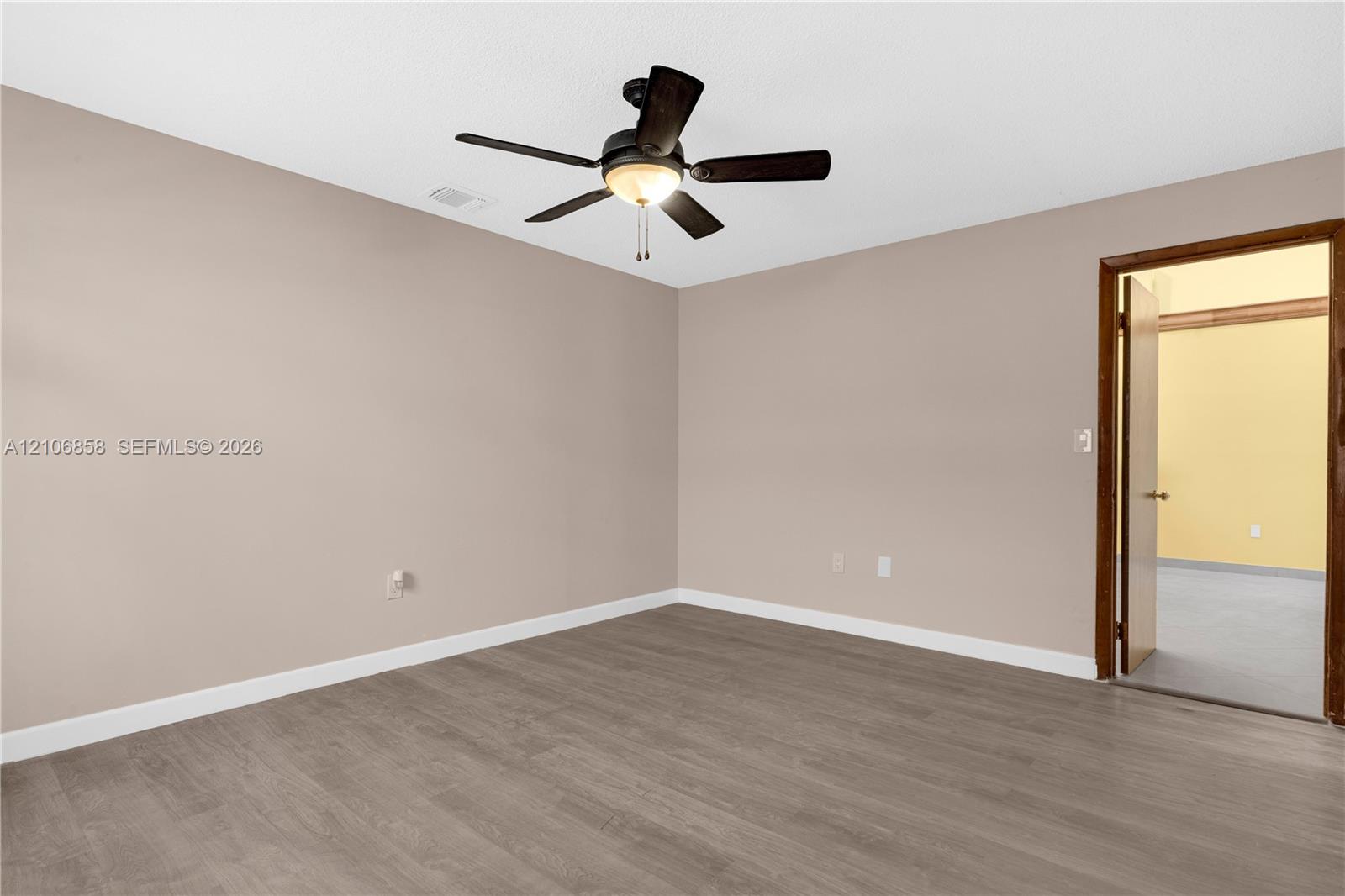 Interior room featuring wood-finish flooring, neutral wall paint, and a central ceiling fan with integrated lighting