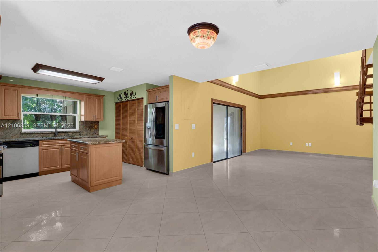Kitchen featuring natural wood cabinetry, stone countertops, central island, stainless steel refrigerator, and tiled flooring