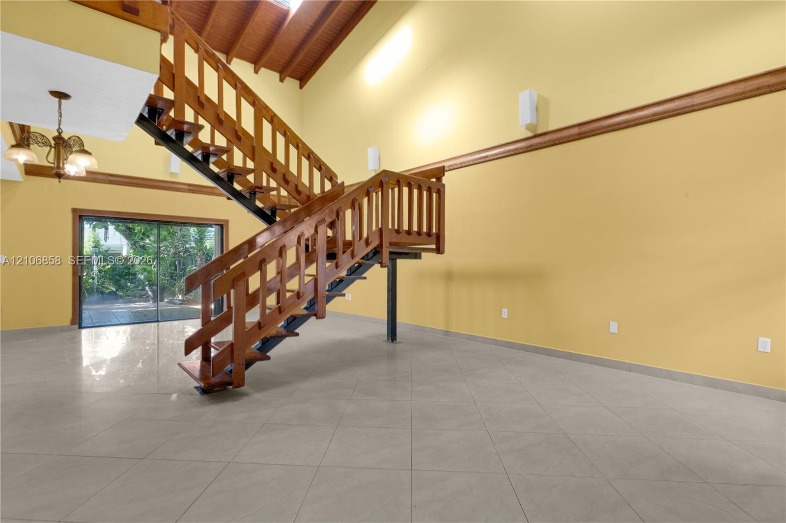Vaulted ceiling with exposed wood-beam detailing, open-tread staircase with wood railings, large-format tile flooring, and oversized sliding glass doors Vaulted ceiling with exposed wood-beam detailing, open-tread staircase with wood railings, large-format tile flooring, and oversized sliding glass doors