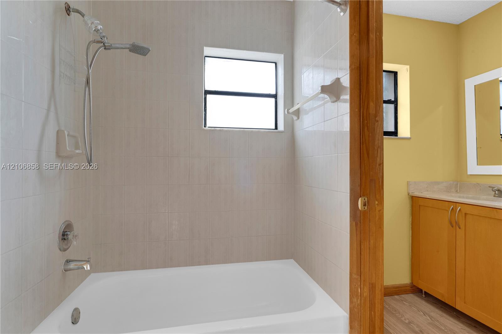 Bathroom featuring a tub-shower combination with light-toned ceramic tile surround, a hand-held showerhead, and a vanity cabinet with a solid surface countertop
