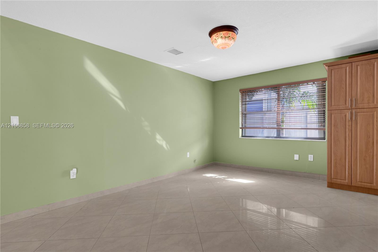 Room featuring large-format tile flooring, built-in wooden cabinetry, and a window with horizontal blinds
