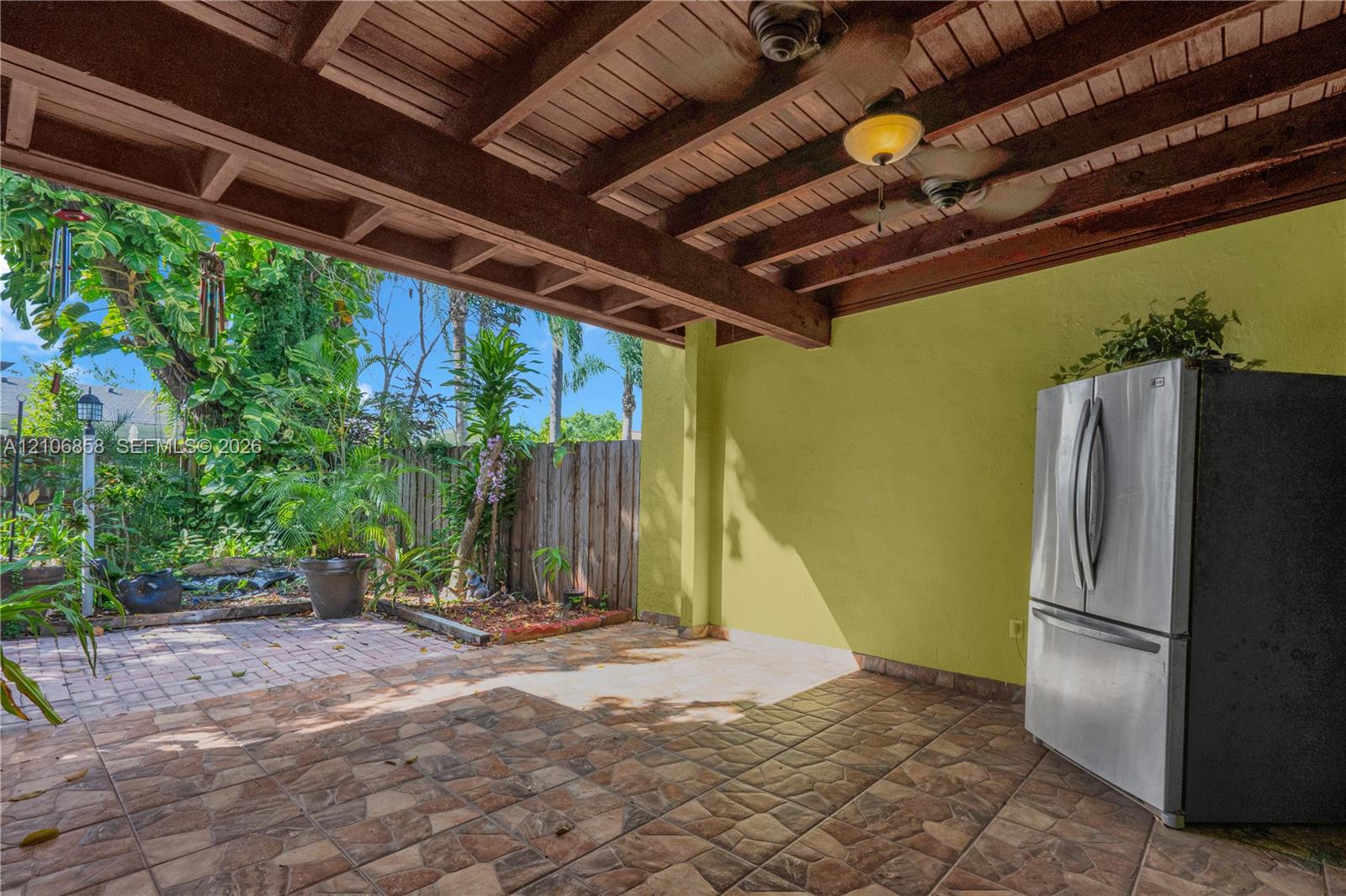 Covered patio featuring an exposed wood-beam ceiling with mounted ceiling fans, tiled flooring, built-in stainless steel refrigerator, and hardscaped brick detailing