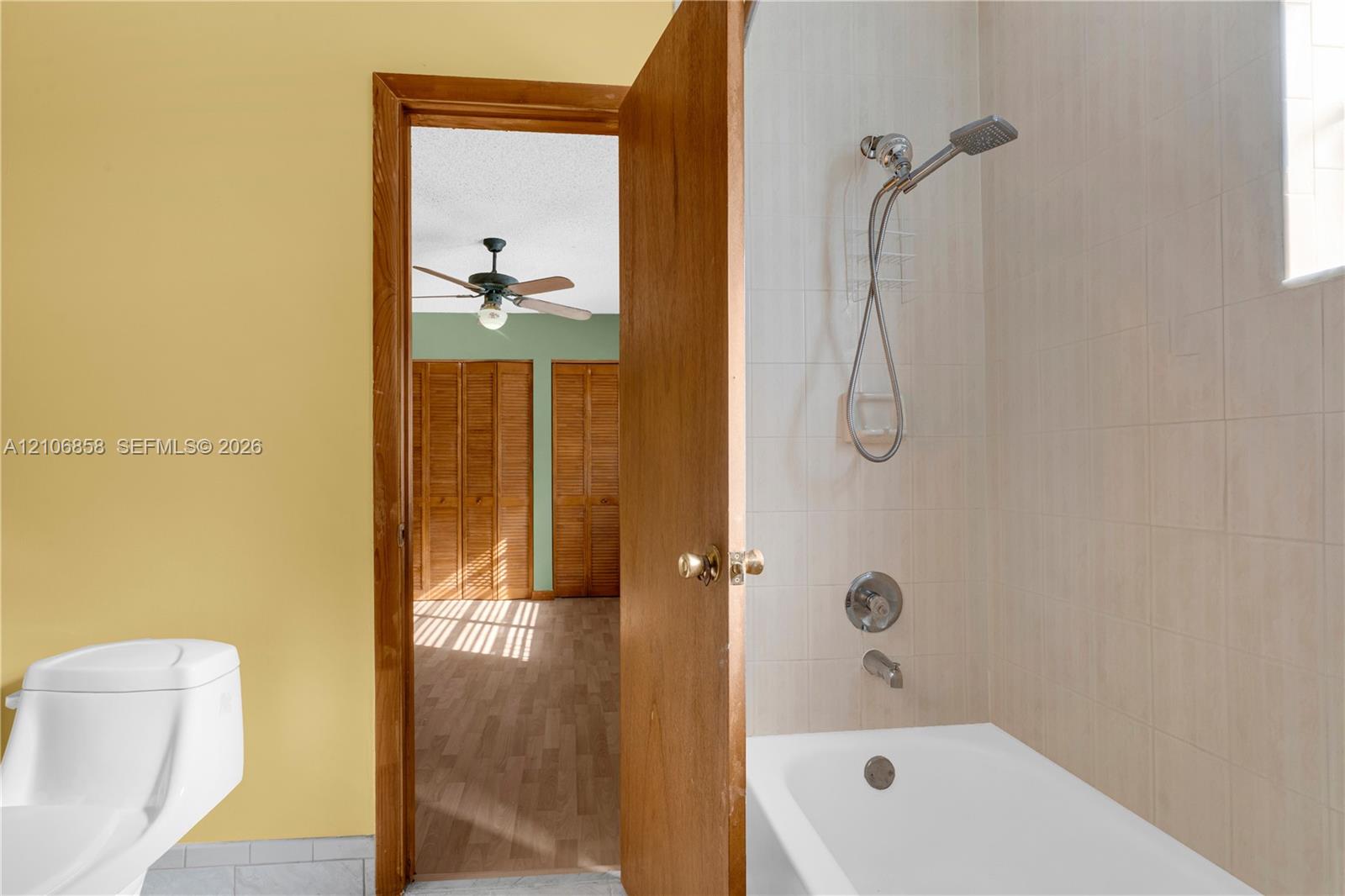 Bathroom featuring a white bathtub with a handheld shower fixture and tiled surround, accompanied by a white toilet