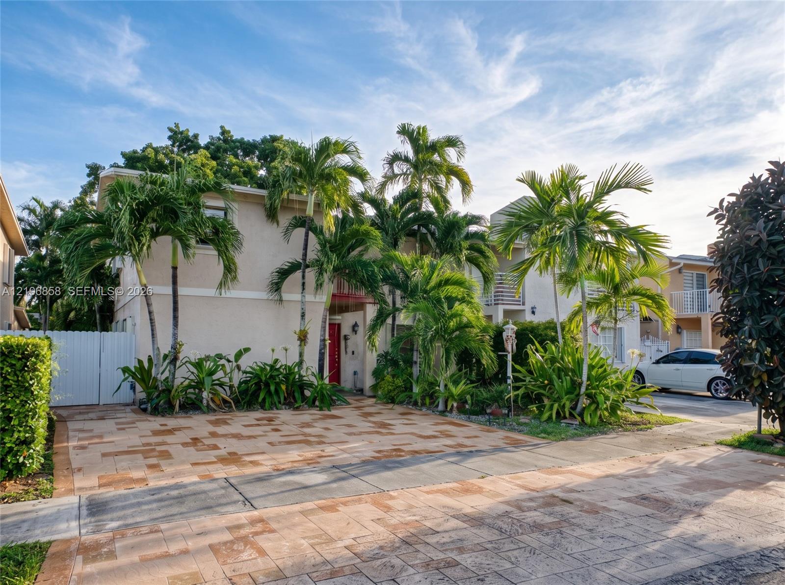 Multi-level exterior featuring a smooth stucco finish, paved driveway, second-story balcony, and established palm trees Multi-level exterior featuring a smooth stucco finish, paved driveway, second-story balcony, and established palm trees