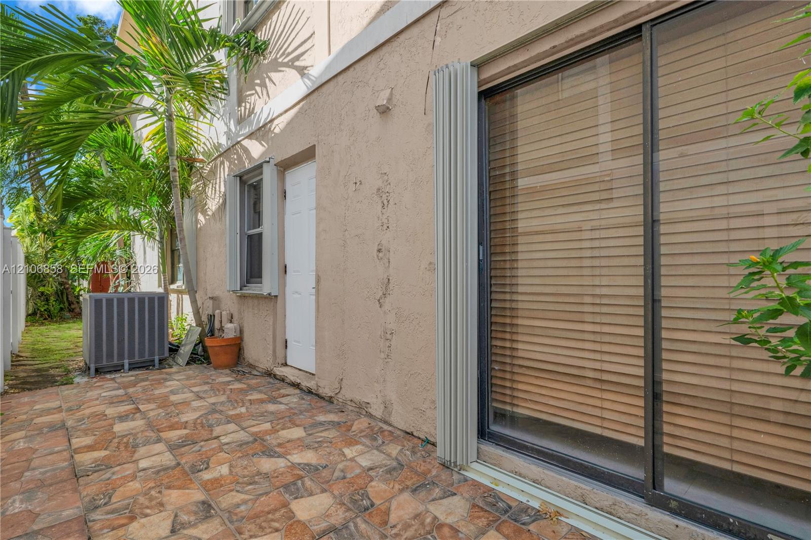 Exterior patio featuring multi-toned tile flooring, stucco wall finish, sliding glass doors, and a pedestrian door