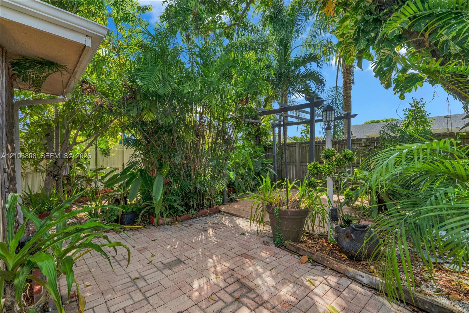 Brick paver patio featuring a wooden pergola, privacy fencing, and lush tropical landscaping