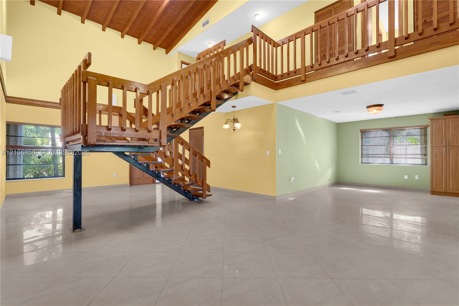 Vaulted wood-plank ceiling, structural metal staircase with wood railing, mezzanine balcony, large-format tile flooring, and built-in cabinetry Vaulted wood-plank ceiling, structural metal staircase with wood railing, mezzanine balcony, large-format tile flooring, and built-in cabinetry