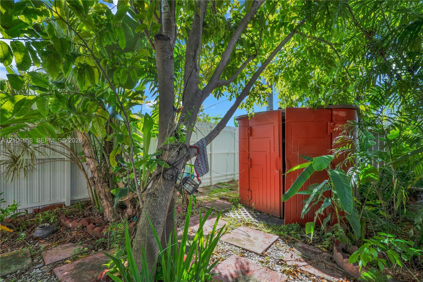 Private backyard featuring mature landscaping, a circular storage structure, stone paver pathway, and solid perimeter fencing