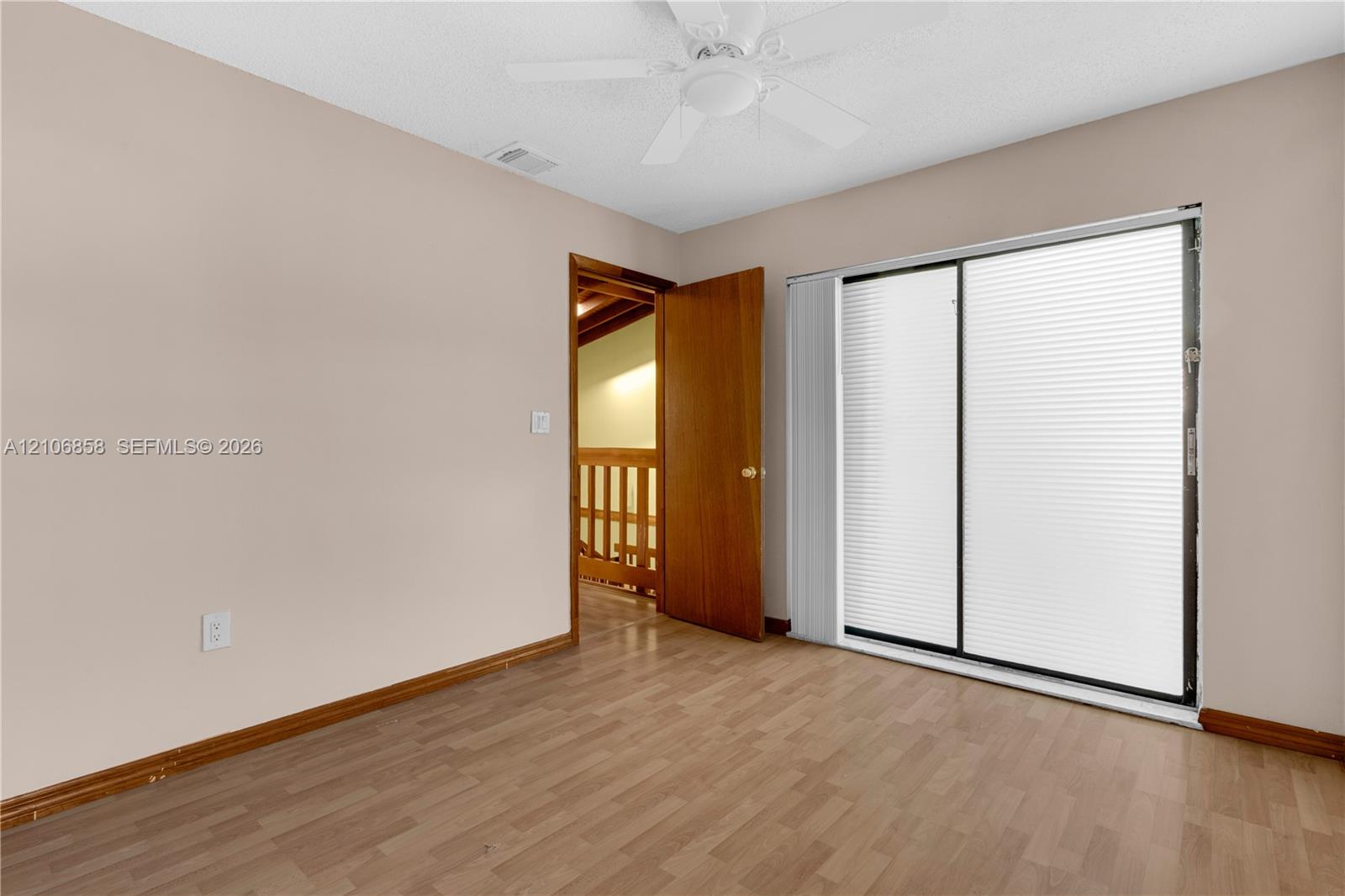 Interior room featuring wood-finish flooring, a ceiling fan, and sliding glass doors with integrated blinds