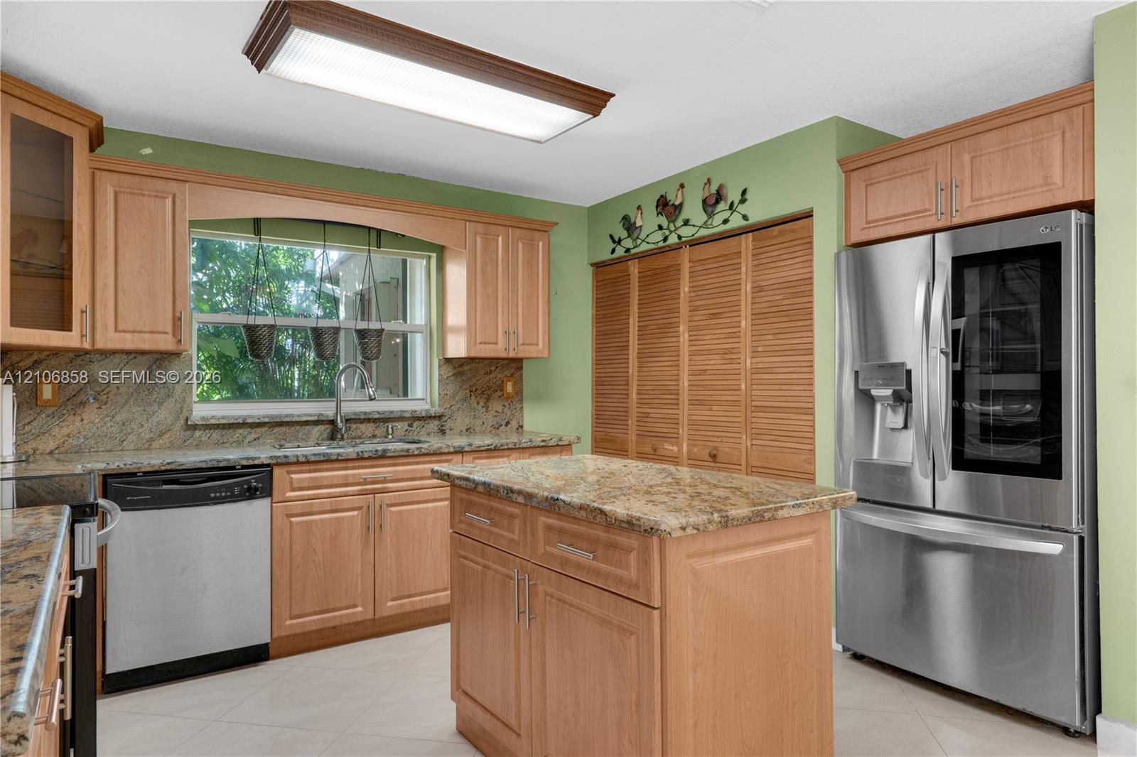 Kitchen featuring natural wood cabinetry, stone-surface countertops, stainless steel appliances, a central island, and louvered built-in pantry doors Kitchen featuring natural wood cabinetry, stone-surface countertops, stainless steel appliances, a central island, and louvered built-in pantry doors