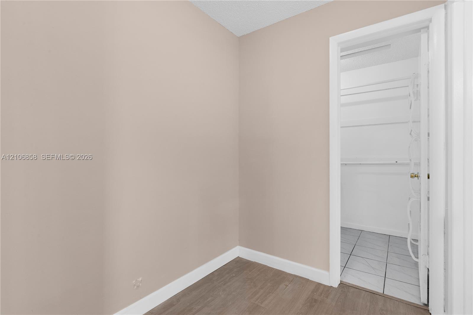 Neutral-toned interior featuring wood-finish flooring, white door casing, and a reach-in storage area with built-in shelving and light-colored tile flooring