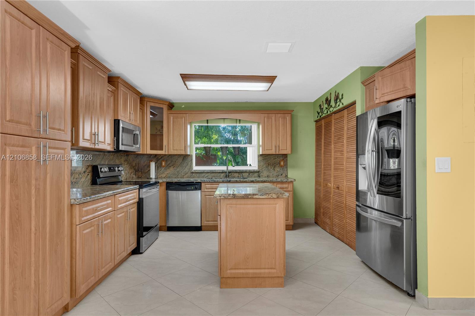 Kitchen featuring wood cabinetry, stone countertops, stainless steel appliances, a center island, and tile flooring Kitchen featuring wood cabinetry, stone countertops, stainless steel appliances, a center island, and tile flooring