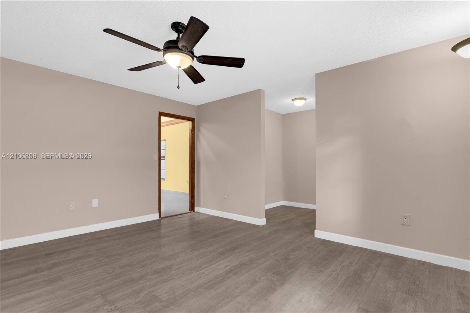 Interior space featuring neutral-toned walls, wood-finish flooring, a five-blade ceiling fan with integrated lighting, and multiple flush-mount ceiling light fixtures