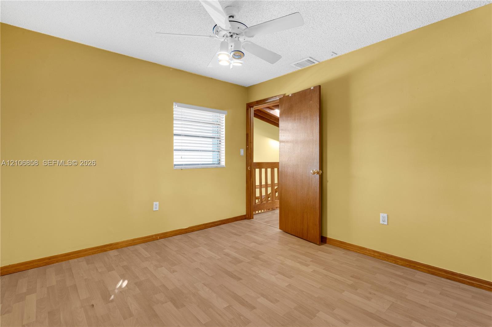 Room featuring wood-finish flooring, a white ceiling fan with integrated lighting, and a window with horizontal blinds