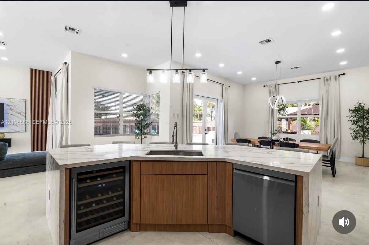 Kitchen island featuring a waterfall-edge countertop, undermount stainless steel sink, wood-finish cabinetry, built-in wine refrigerator, and stainless steel dishwasher