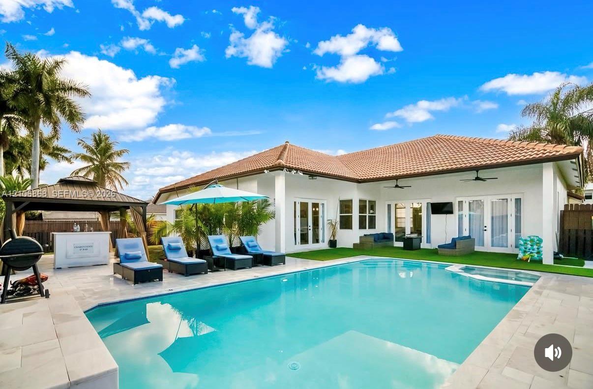 Outdoor area featuring an in-ground swimming pool with an integrated spa, stone-paver decking, and a permanent metal-roofed pavilion Outdoor area featuring an in-ground swimming pool with an integrated spa, stone-paver decking, and a permanent metal-roofed pavilion