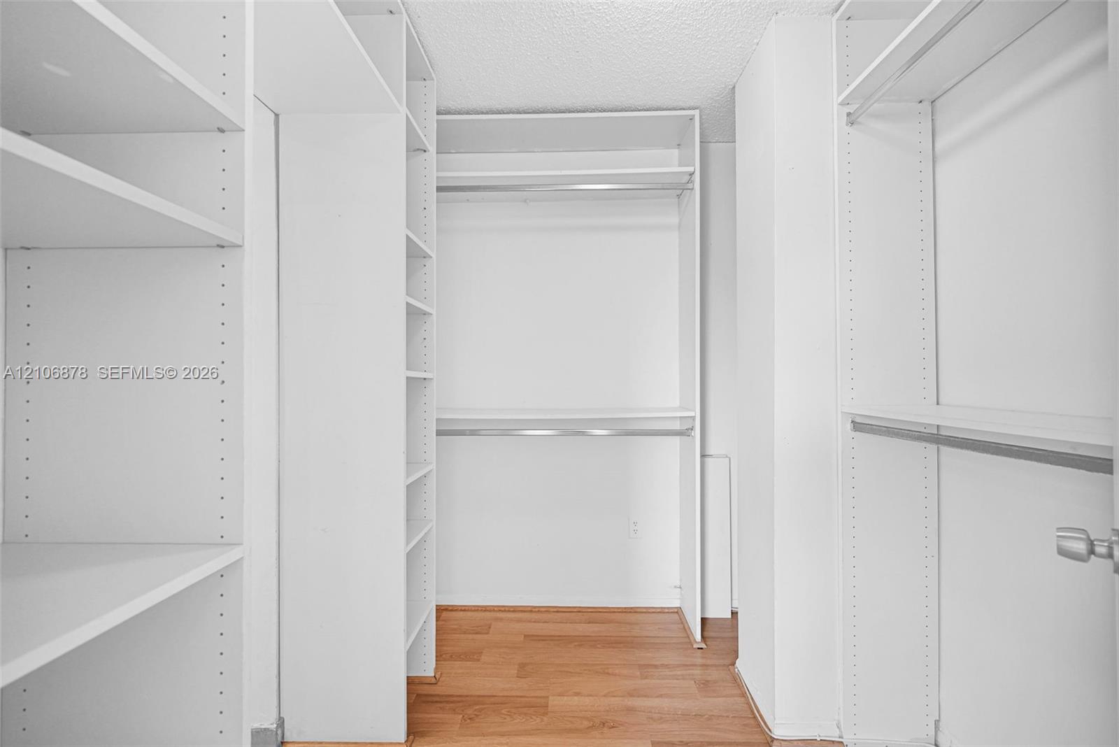Walk-in closet featuring white built-in shelving, multiple hanging rods, and wood-finish flooring