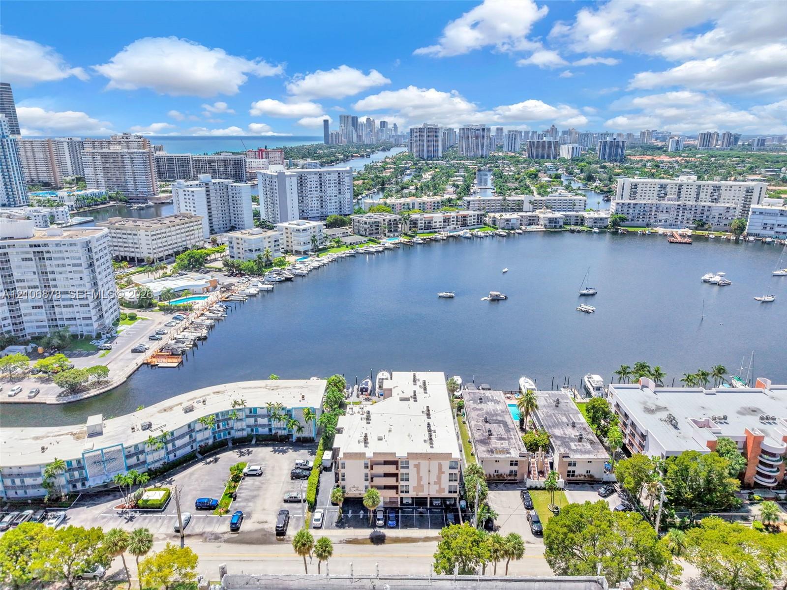 Aerial perspective of the property featuring a waterfront location, expansive canal exposure, paved surface parking, and proximity to regional coastal landmarks