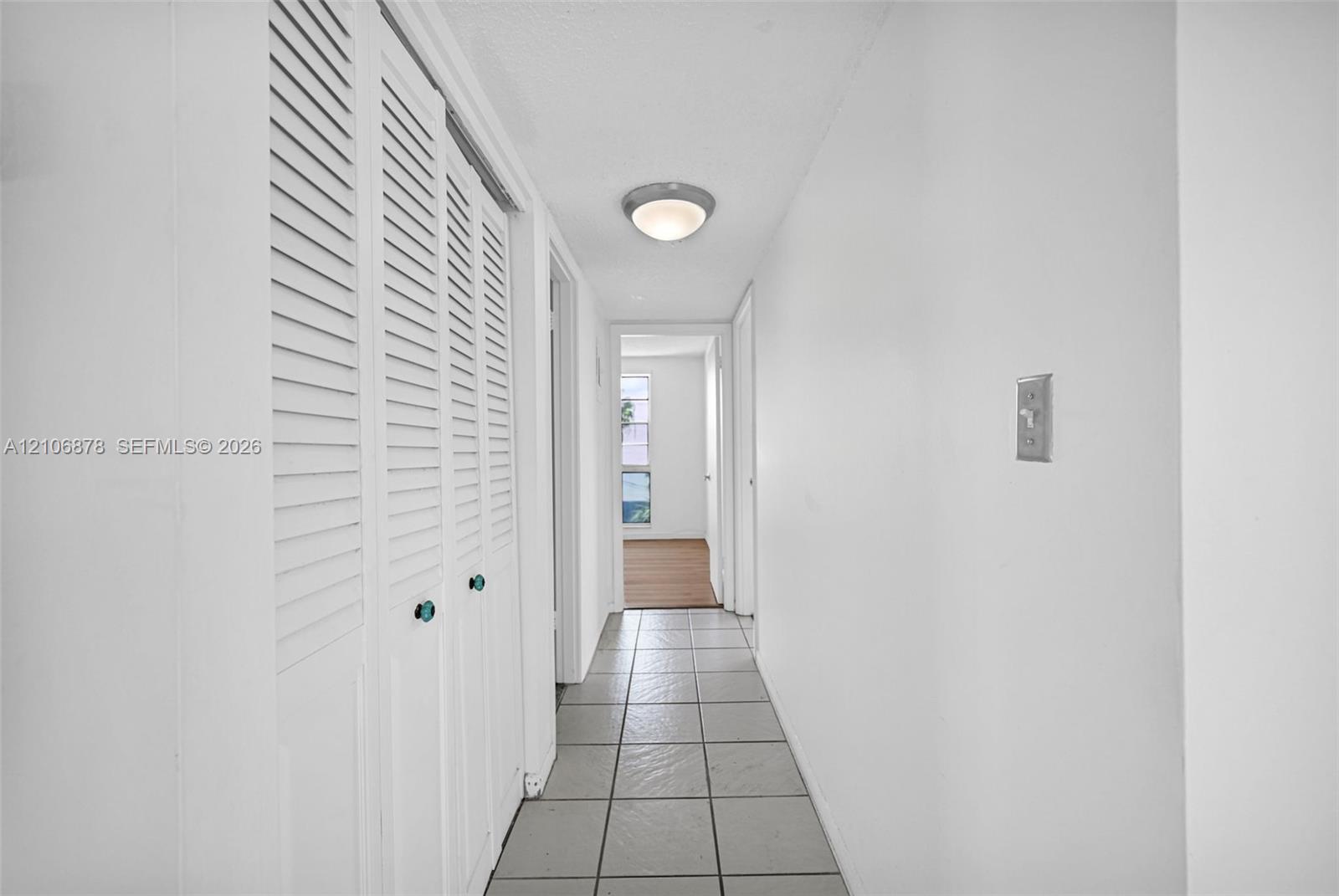 Hallway featuring tile flooring, white louvered closet doors, and a flush-mount ceiling light fixture