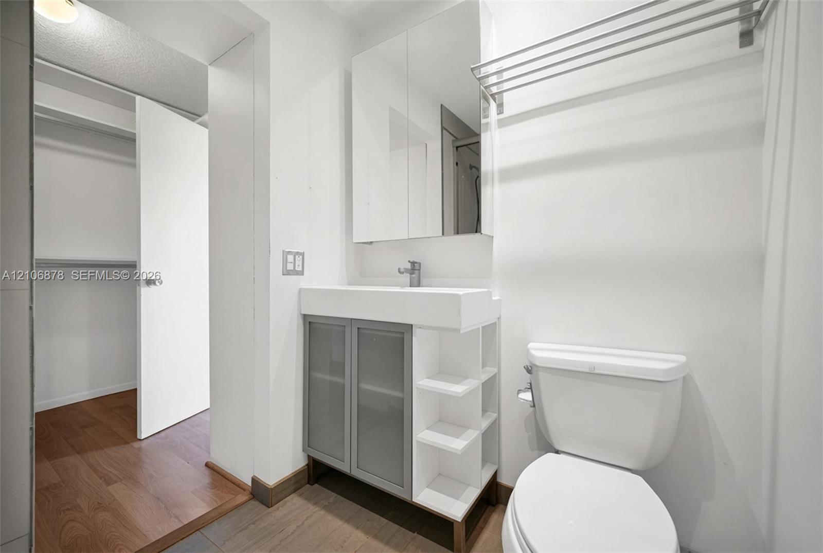 Bathroom featuring a vanity with frosted glass cabinet doors, open shelving, and an integrated basin, paired with a mirrored medicine cabinet and a wall-mounted metal towel rack