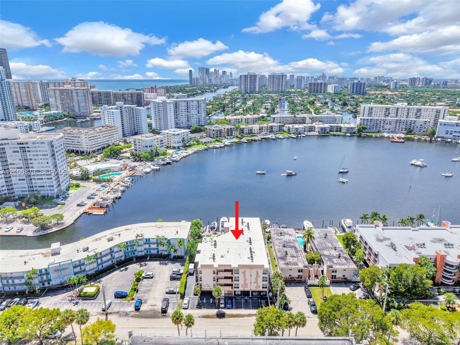 Aerial perspective of multi-story residential building featuring waterfront positioning and dedicated ground-level parking