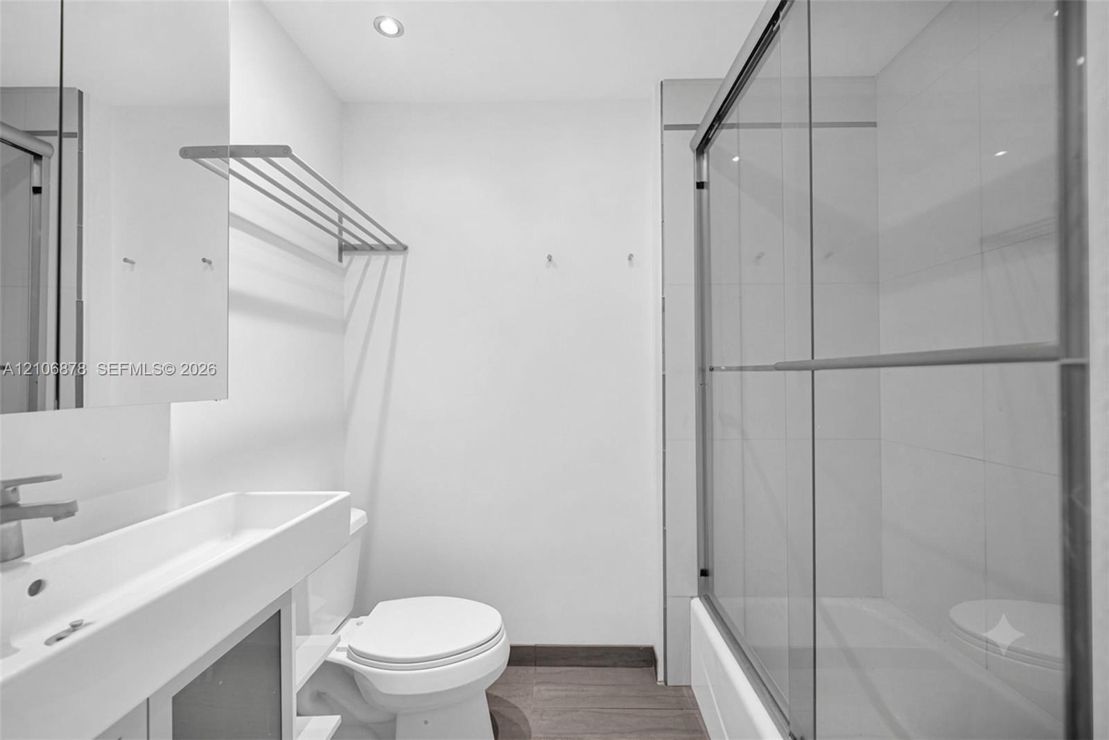 Modern bathroom featuring a trough-style sink, chrome wall-mounted faucet, wood-finish flooring, and a glass-enclosed shower with wall-mounted towel rack