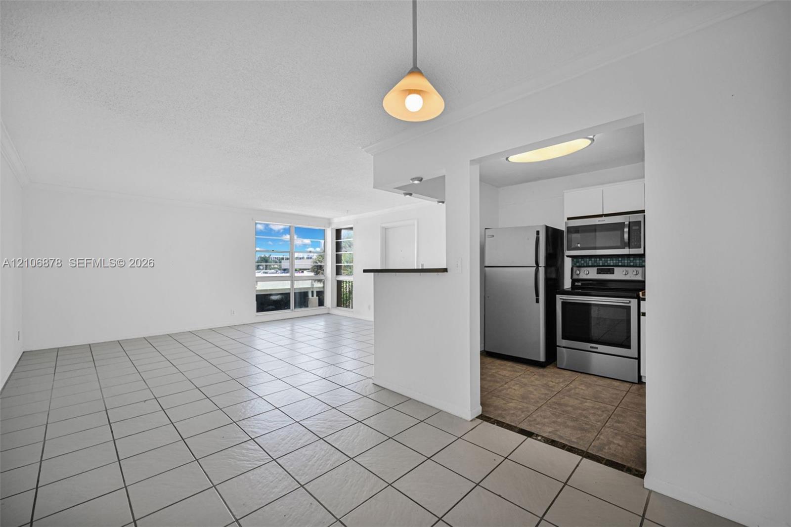 Open living area featuring neutral tile flooring, breakfast bar, stainless steel kitchen appliances, and large windows