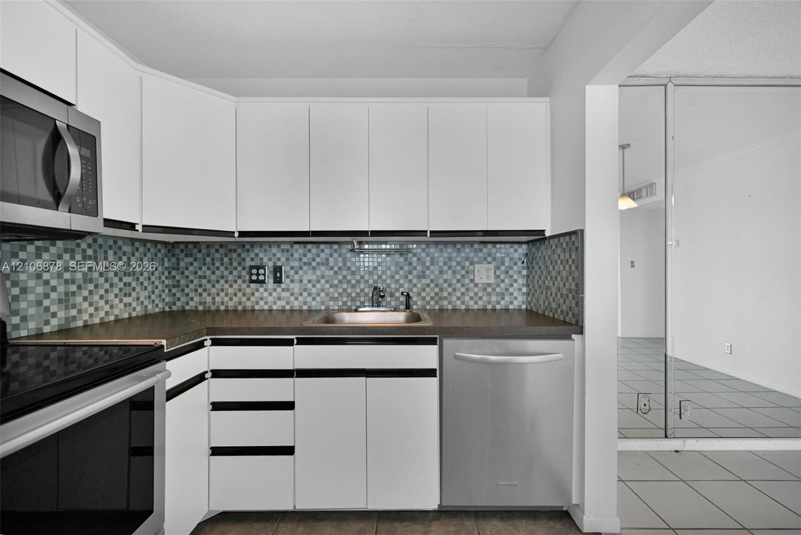 Kitchen featuring white cabinetry with black accents, mosaic tile backsplash, stainless steel appliances, and a single-basin sink