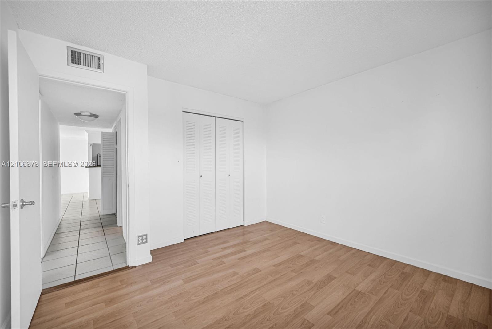 Interior room featuring wood-finish flooring, white walls, and a closet with bifold doors