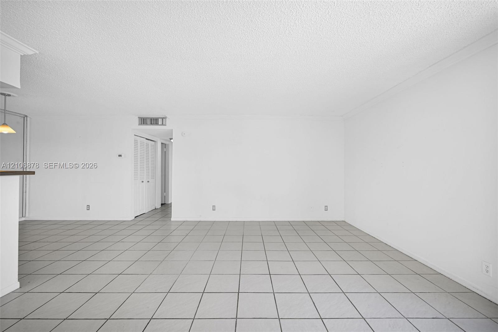 Open-concept interior featuring neutral ceramic tile flooring, a textured ceiling, and louvered-style closet doors