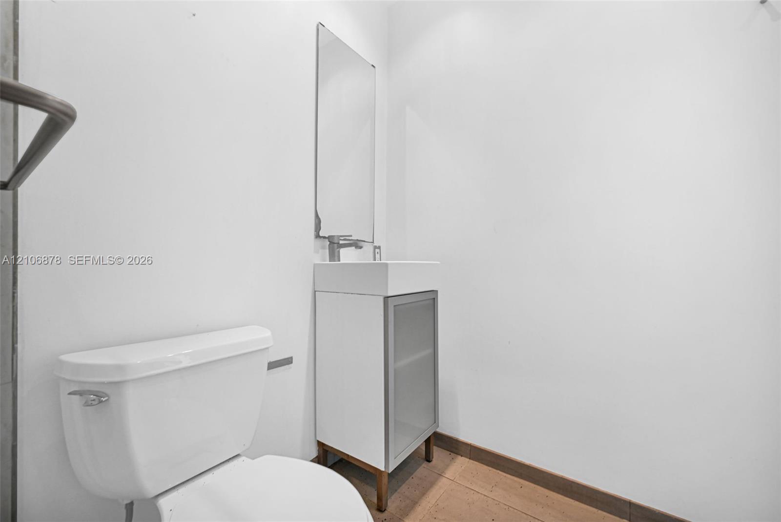 Wall-mounted mirror, pedestal-style vanity with a frosted glass cabinet door, rectangular sink basin, metallic faucet, and toilet