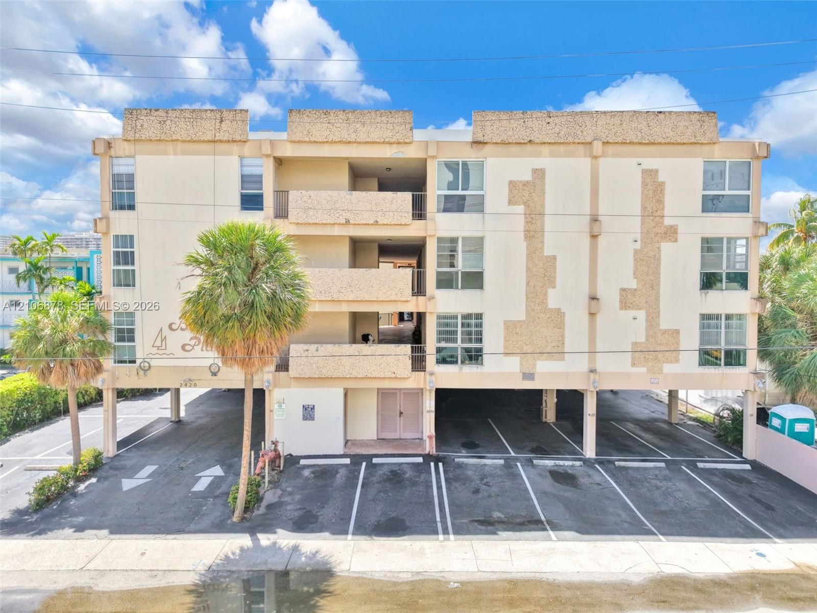 Multi-story building exterior featuring textured masonry accents, private balconies, covered ground-level parking, and metal-frame windows