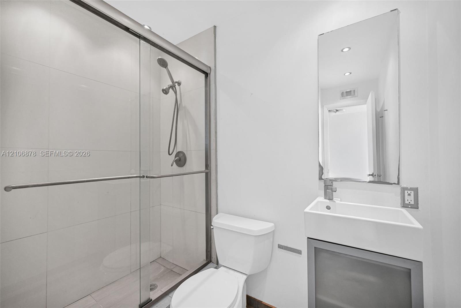 Walk-in shower with sliding glass door, white wall tiling, wall-mounted handheld shower fixture, rectangular vessel sink on a metal-frame vanity, and a rectangular mirror
