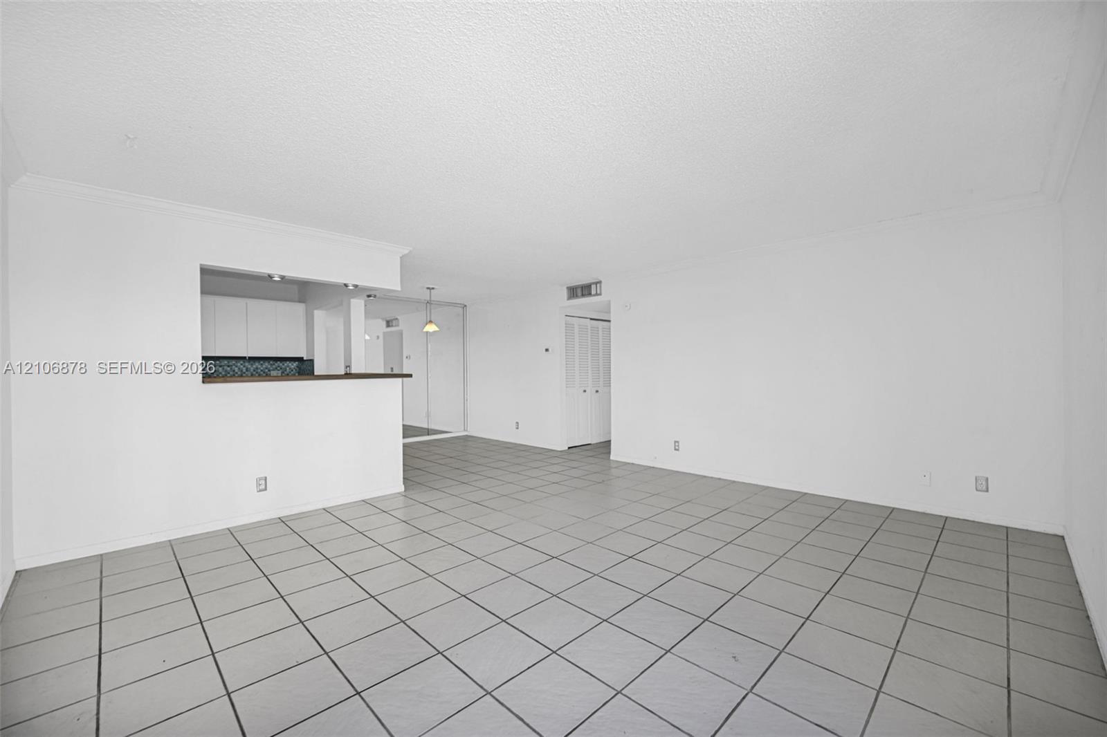 Open living area featuring neutral tile flooring, a pass-through opening, and white cabinetry