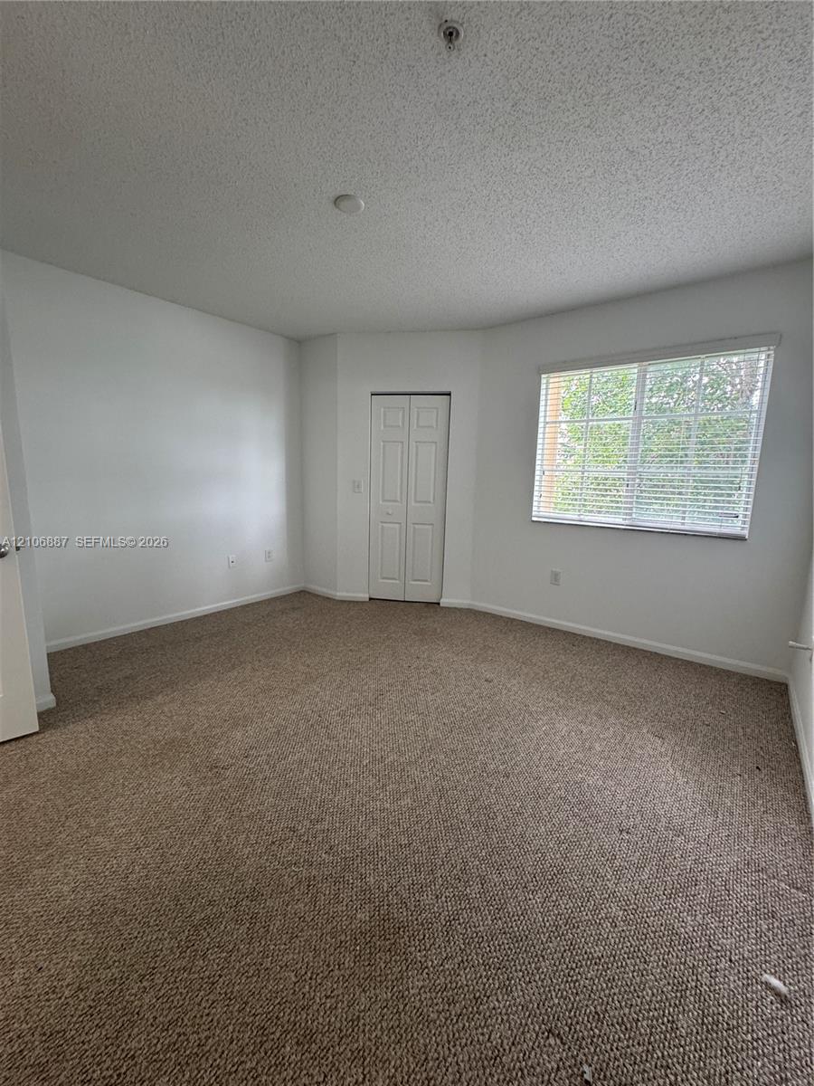 Neutral-toned carpeting, textured ceiling, window with blinds, and dual-panel closet doors