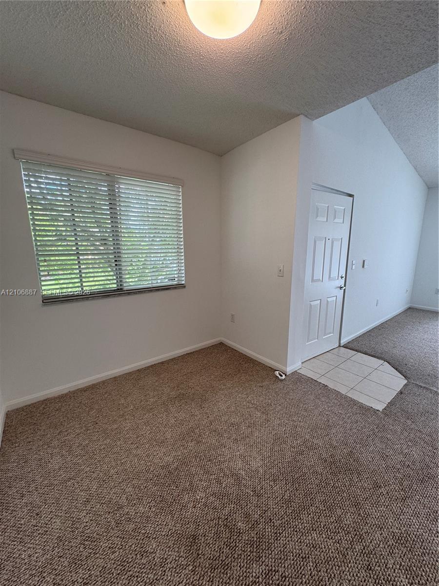 Interior area featuring vaulted ceilings, textured wall finishes, neutral carpeting, a tiled entryway, and horizontal window blinds