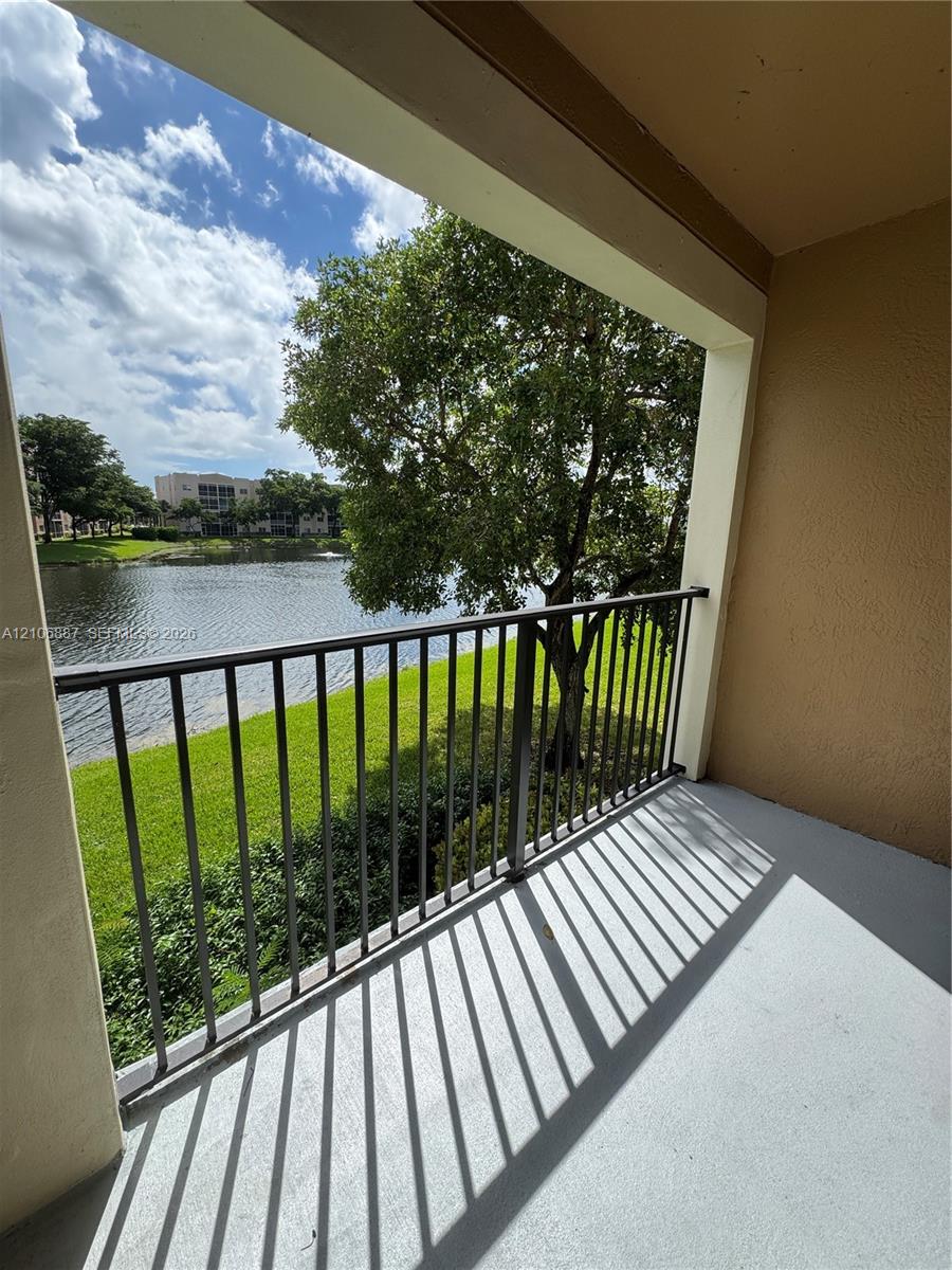 Covered balcony featuring a metal railing, concrete flooring, and water frontage with mature landscaping