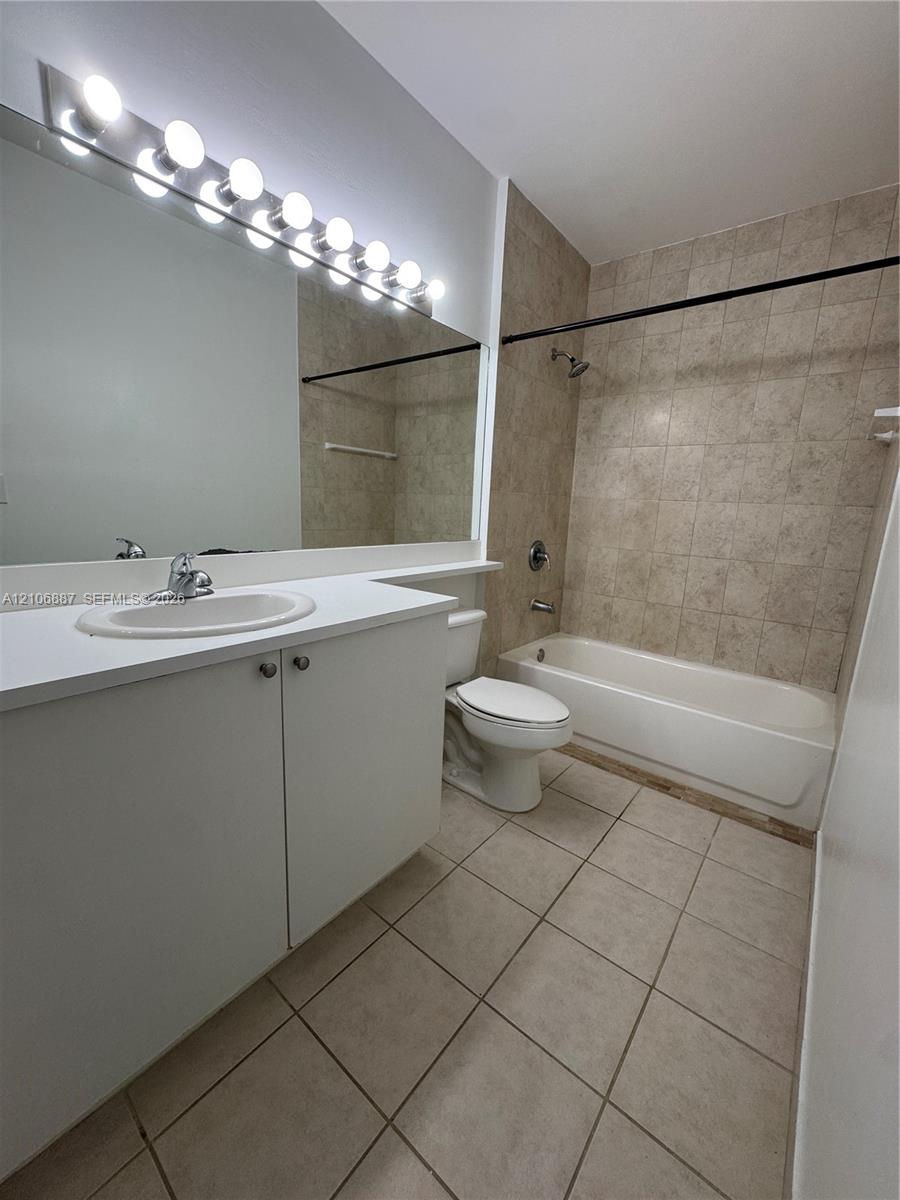 Bathroom featuring a vanity with white cabinetry, a neutral countertop, an integrated sink, a full-width wall mirror with integrated lighting, and a tub-shower combination with tile surround