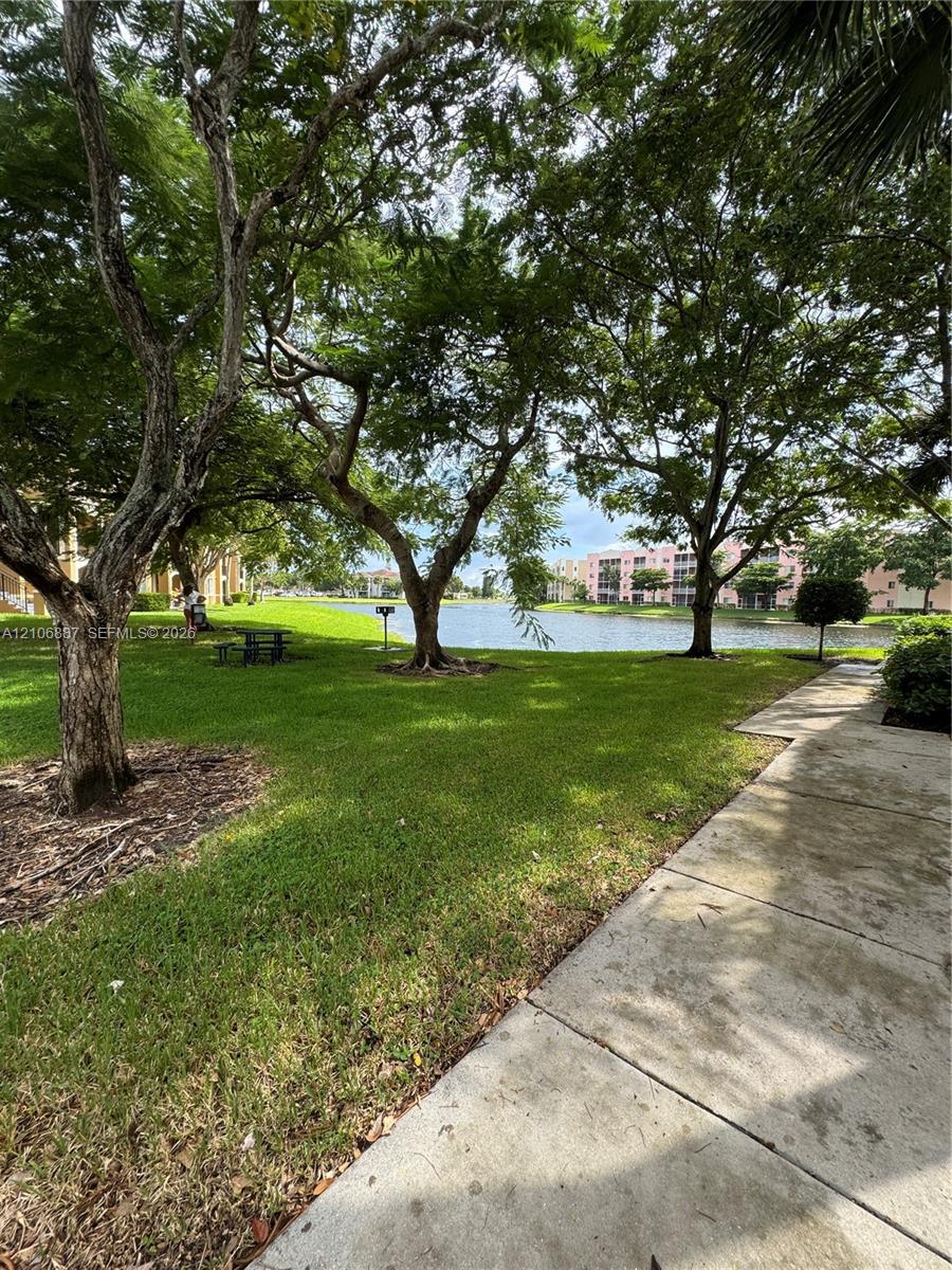 Grounds featuring mature shade trees, expansive grass lawn, concrete walkway, and waterfront exposure