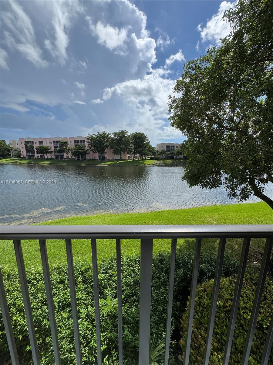Metal balcony railing overlooking a lake, expansive grass lawn, and mature trees