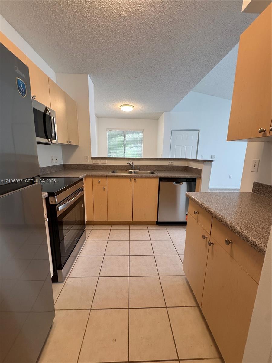 Kitchen featuring light-finish cabinetry, neutral stone-textured countertops, stainless steel appliances, and ceramic tile flooring