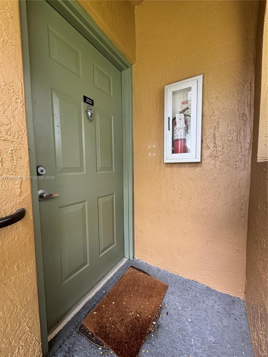 Solid core door featuring a polished metal lever handle, deadbolt lock, and recessed panel detailing, paired with a wall-mounted glass-enclosed fire extinguisher cabinet