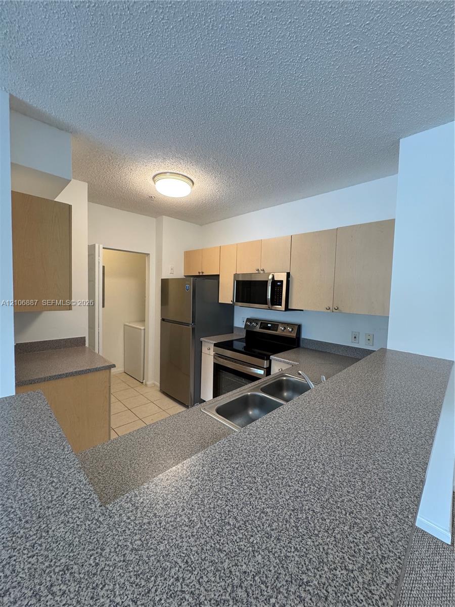 Kitchen featuring light-finish cabinetry, speckled countertops, stainless steel appliances, and a dual-basin stainless steel sink