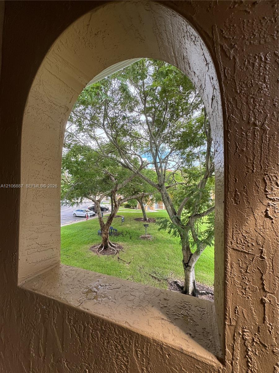 Arched architectural window opening with a textured stucco finish, framing a landscape featuring mature trees and a grass lawn
